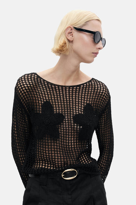 Pull noir avec col rond de MANGO, avec des détails floraux et porté avec un pantalon noir et une ceinture.