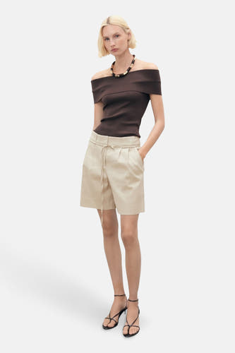 Shorts beige de MANGO, portés avec un haut marron à épaules dénudées, des baskets noires et une chaîne.