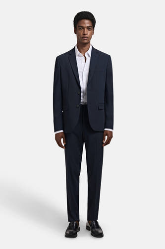 Chemise blanche à manches longues de MANGO, portée avec un pantalon bleu marine et des chaussures noires.