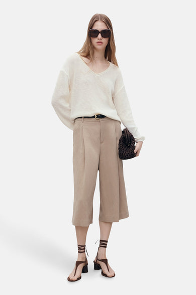T-shirt à col V blanc de MANGO, porté avec des culottes beige, des sandales brunes à brides et un sac à main brun.
