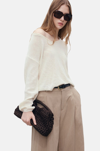 Pull blanc à col V de MANGO, porté avec une poche main marron et un ceinture.