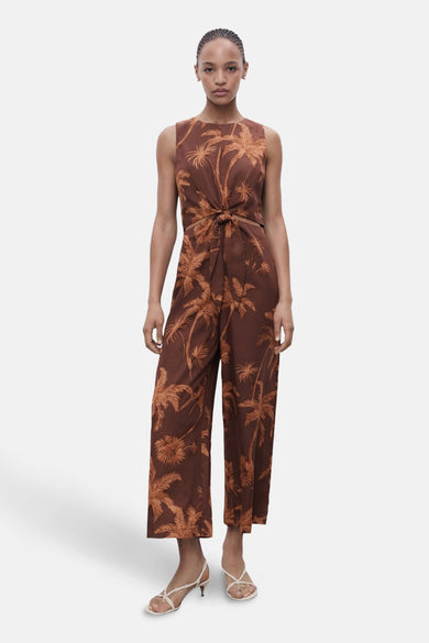 Combinaison brune de MANGO avec imprimé palmier et détail de bouton à l'avant, portée avec des sandales blanches.