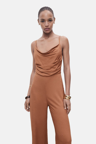 Combinaison brune de MANGO, avec une ligne de col drapée et des bracelets dorés.