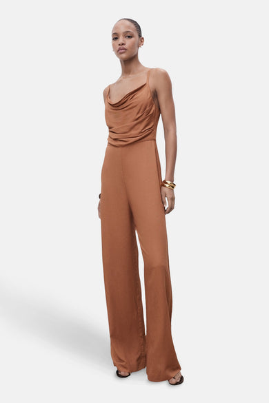 Combinaison marron de MANGO avec une ligne de col drapée et des manches larges, associée à des bracelets dorés.