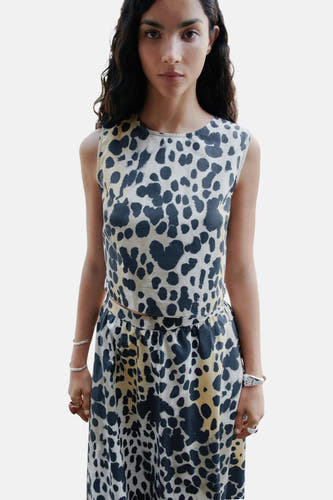 Blouse sans manches beige de MANGO, avec une impression tachetée noire et portée avec une jupe coordonnée.