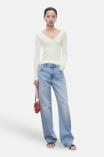Pull blanc à col rond de MANGO, associé à des jeans larges et un sac rouge frangé.