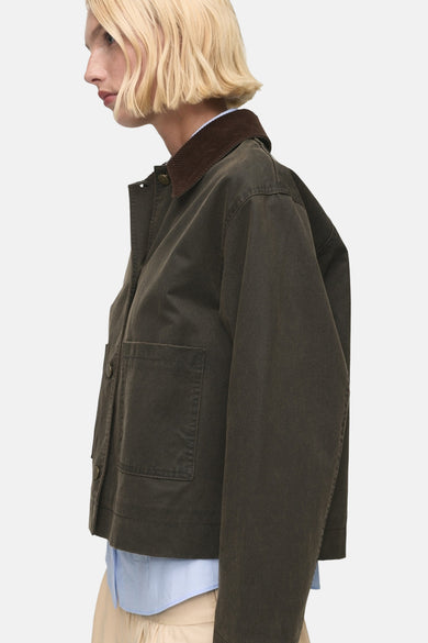 Veste kaki courte de MANGO, avec une collet brune et un chemisier bleu visible en dessous, en vue latérale.
