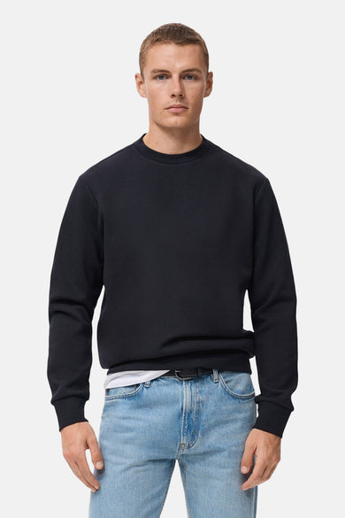 Pull-over bleu avec col rond de MANGO, porté sur un t-shirt blanc et des jeans bleus à ce.