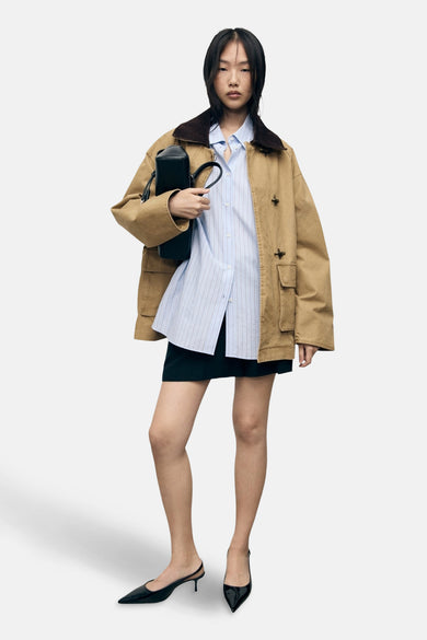 Manteau court beige de MANGO, avec une collier marron porté sur un chemisier rayé bleu et une jupe noire.
