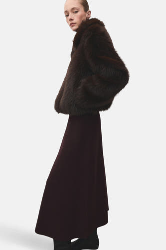 Longue jupe bordeaux de MANGO, associée à une veste en fourrure marron foncé et des chaussures noires.