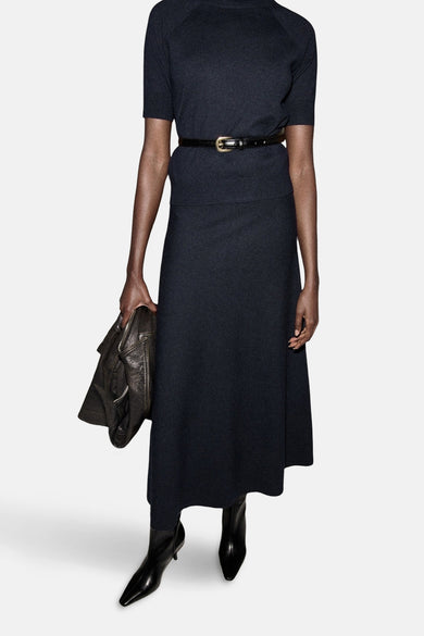 Long manteau bleu de MANGO, avec une fine ceinture et associé à des bottes noires.