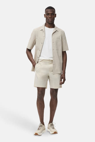 Chemise beige à manches courtes de MANGO, portée avec un T-shirt blanc et des short beige.