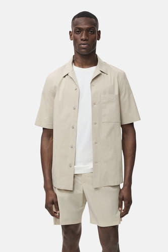 Chemise beige à manches courtes de MANGO, portée sur un T-shirt blanc et des shorts coordonnés.