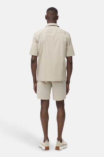 Chemise beige à manches courtes de MANGO, vue de derrière, avec des shorts et des sneakers assortis.