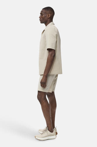 Chemise beige à manches courtes de MANGO, associée à des shorts et des sneakers coordonnés, en vue latérale.