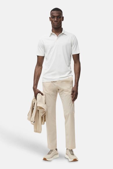 Polo écru à manches courtes de MANGO, porté avec un pantalon beige, des sandales et un manteau sur le bras.