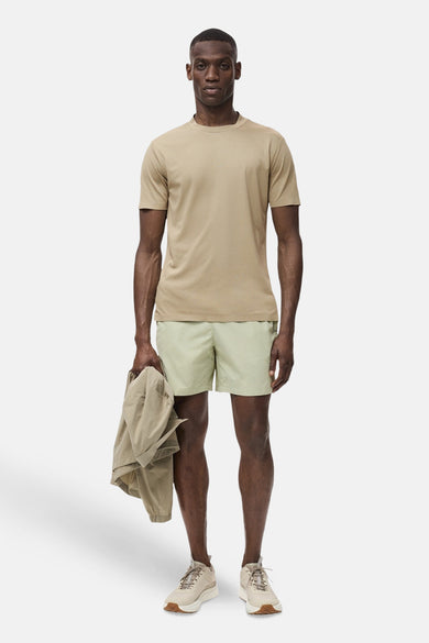 T-shirt beige à manches courtes de MANGO, porté avec des shorts verts clairs et des chaussures décontractées.