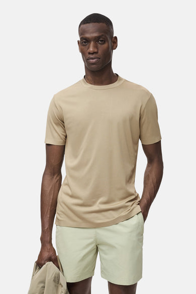T-shirt beige avec manches courtes de MANGO, porté avec des shorts verts clairs et un manteau beige dans la main.