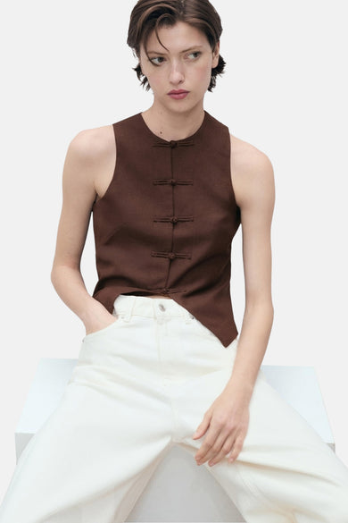 Blazer marron de MANGO avec fermeture à boutons chinois, porté avec un pantalon blanc.
