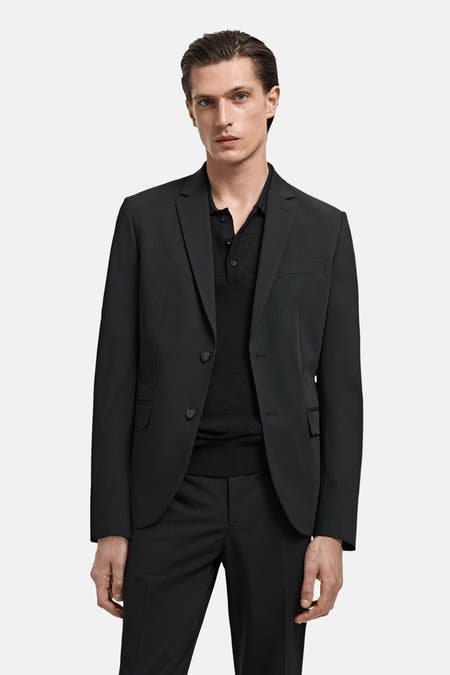 Blazer noir de MANGO, porté avec un t-shirt noir et un pantalon.