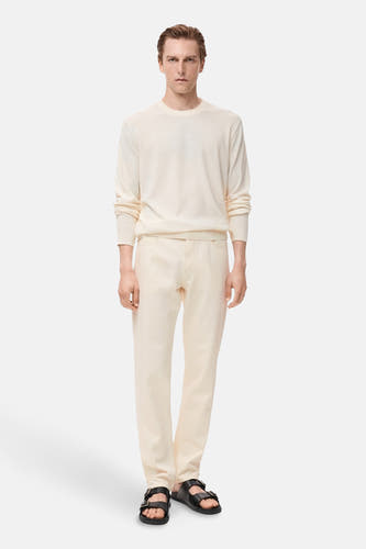 T-shirt écru avec col rond de MANGO, associé à un pantalon beige et des sandales noires.