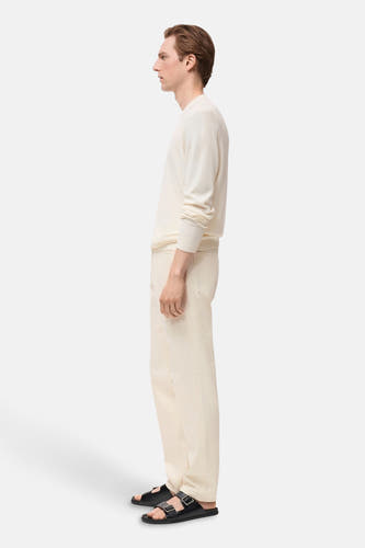 T-shirt écru avec col rond de MANGO, à manches longues, porté avec un pantalon crème et des sandales noires, vue latérale.