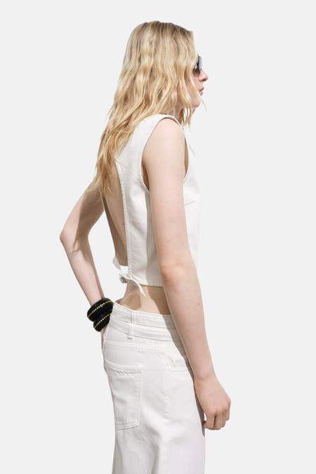 Blouse écru sans manches de MANGO, avec dos nu et détail noué, associée à un jean blanc.