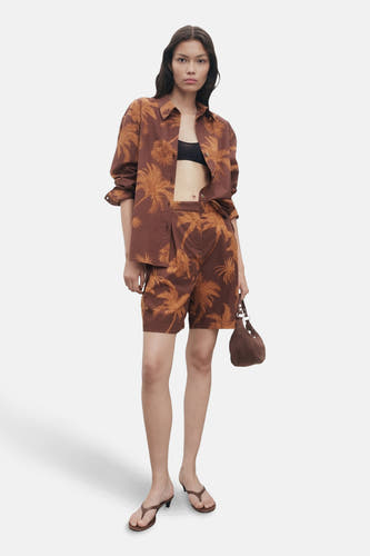 Chemise brune à longues manches de MANGO, avec imprimé palmier, portée avec une short coordonnée et un soutien-gorge noir.