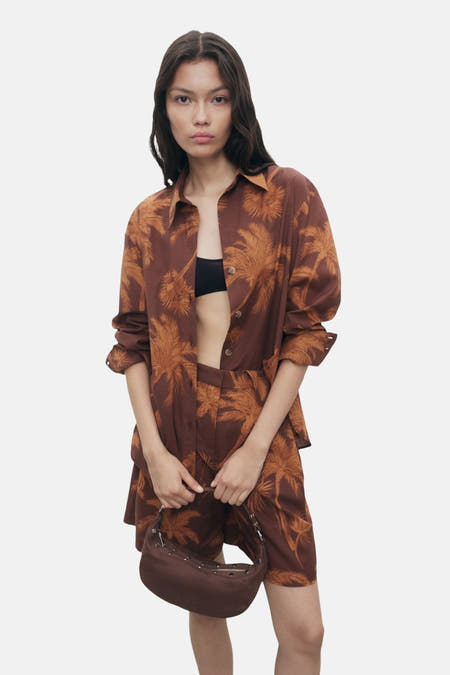 Chemise brune à manches longues de MANGO, avec une impression de palmiers bruns, portée avec un soutien-gorge noir.