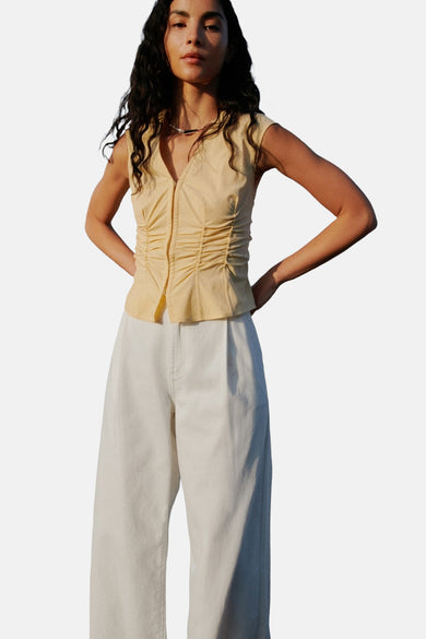 Blouse sans manches MANGO de couleur jaune, avec des plis à l'avant, associée à une jupe blanche.