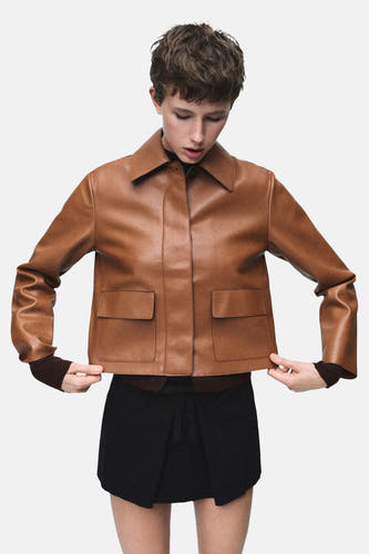 Manteau court brun de MANGO, vu de l'arrière, avec une jupe noire et des chaussettes grises à talons.