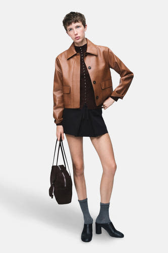 Bruine korte jas van MANGO, gecombineerd met een zwarte rok, grijze sokken, hakken en een bruine tas.