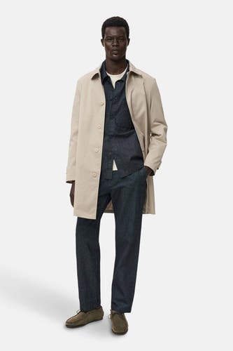 Manteau de denim bleu marine de MANGO, porté sur un T-shirt blanc et associé à un trench coat et des jeans foncés.