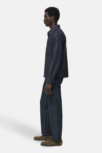 Manteau de denim bleu marine de MANGO, vu de côté, associé à un pantalon coordonné et des chaussures en cuir suédé marron.