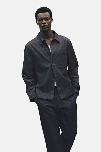 Veste en jeans bleu marine de MANGO, avec des manches longues et une poche poitrine, portée sur un T-shirt blanc.