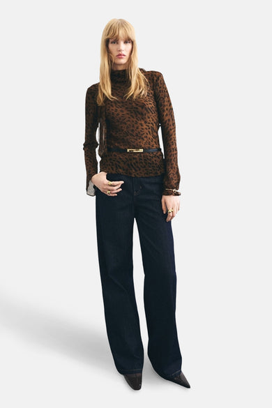 Blouse brune à longues manches de MANGO, avec imprimé animal, associée à des jeans larges foncés, des bagues d'or et une ceinture noire.
