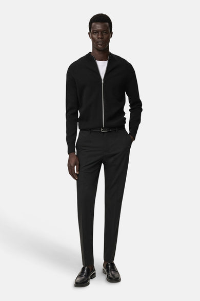 Gilet noir de MANGO, porté sur un T-shirt blanc avec un pantalon noir, une ceinture et des talons en cuir noir.