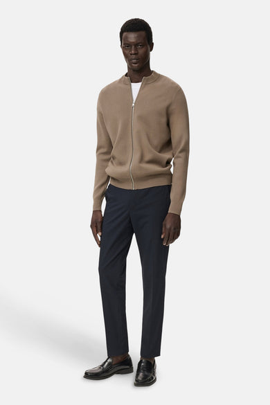 Gilet brun de MANGO porté sur un chemisier blanc avec un pantalon foncé et des loafers noirs.