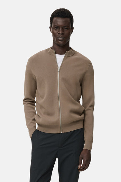 Gilet marron de MANGO, avec des manches longues et une fermeture éclair argentée, porté sur un t-shirt blanc et un pantalon noir.