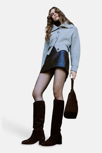 Grijs gilet van MANGO, gedragen met een zwarte leren rok en bruine laarzen, op een lifestyle foto.
