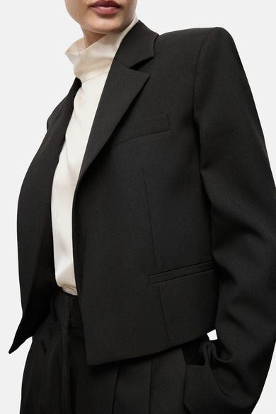 Blazer noir de MANGO, dos, combiné avec une blouse blanche et un pantalon noir.