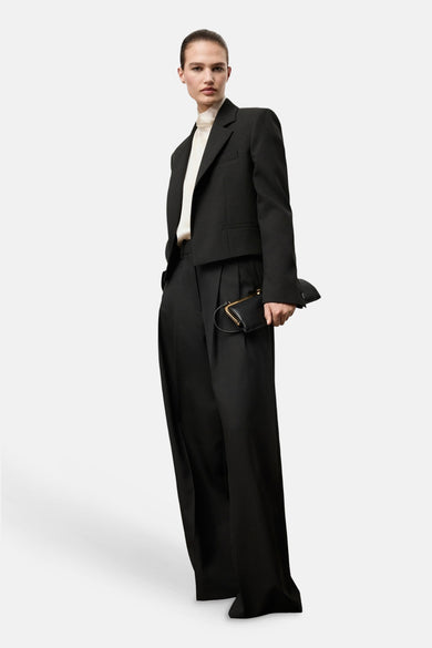 Zwarte blazer van MANGO, gedragen over een crèmekleurige blouse en gecombineerd met een wijde pantalon en een kleine zwarte handtas.
