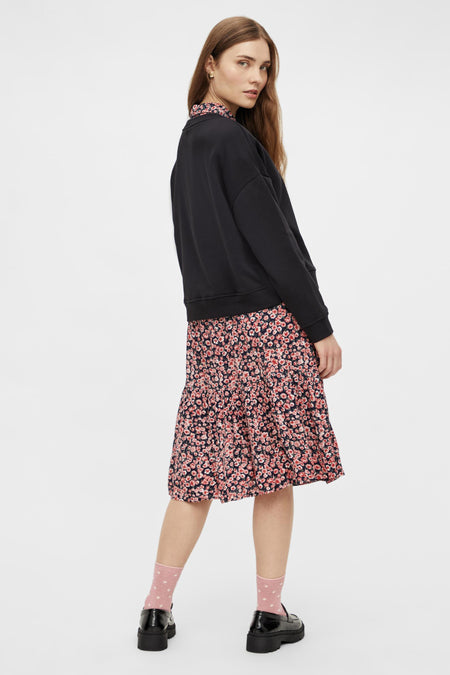 Pull-over noir de PIECES®, porté avec une jupe fleurie, des chaussettes et des loafers.