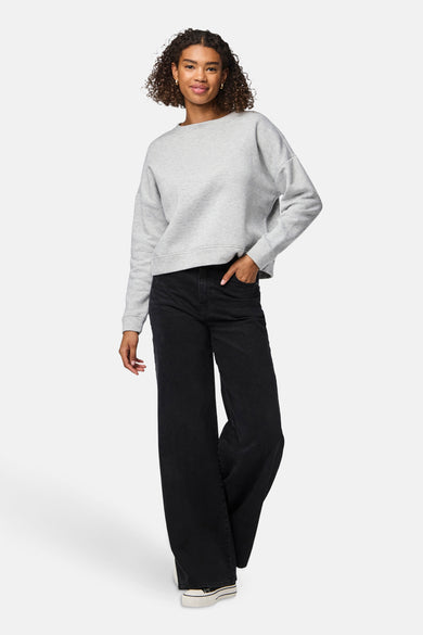 Pull-over gris à col rond de PIECES®, associé à un pantalon noir à larges jambes et des baskets blanches.