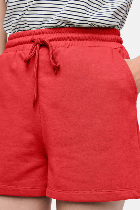Short rouge de PIECES®, avec cordon et une main dans la poche.