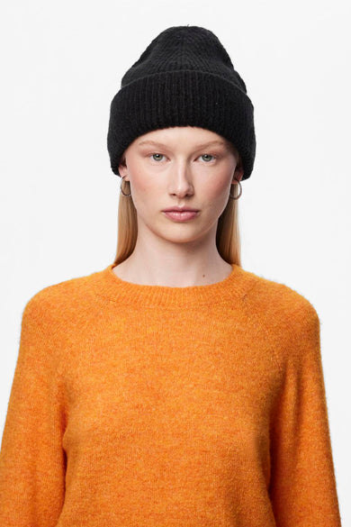 Casquette noire de PIECES, portée avec un pull orange et des boucles d'oreilles en argent.