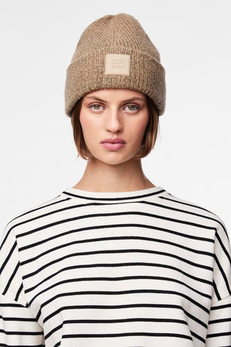 Chapeau beige de PIECES avec une texture côtelée et un patch logo, porté avec un pull rayé.