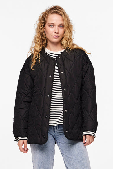 Manteau court noir de PIECES®, à carreaux, porté avec un sac bleu rayé et des jeans déchirés.