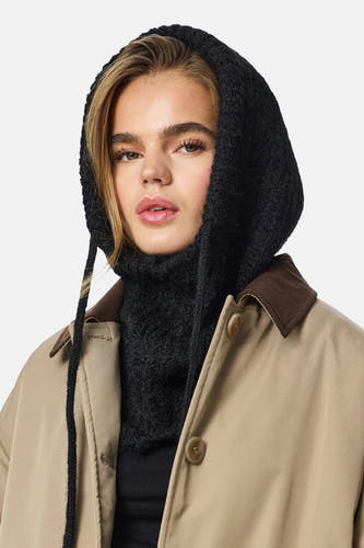 Chapeau noir de PIECES®, avec une texture épaisse tricotée et des cordons, associé à une veste beige avec un col marron.