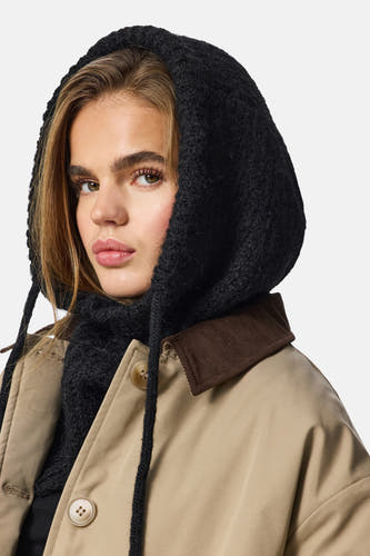 Chapeau noir de PIECES, avec une texture tricotée et des lanières, porté avec un manteau beige à col brun.